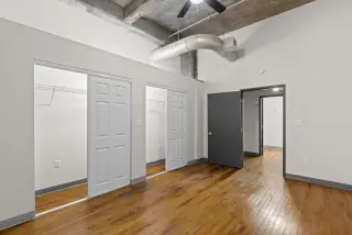 Bedroom with two closets, hardwood floors and exposed ductwork overhead