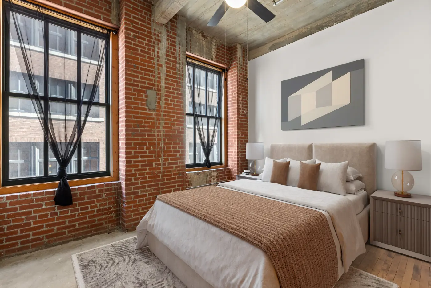 Loft bedroom with brick walls, tall windows and warm textiles