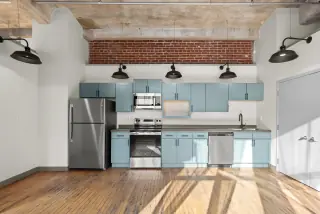 Loft kitchen with soft blue cabinetry, stainless appliances and a brick lintel