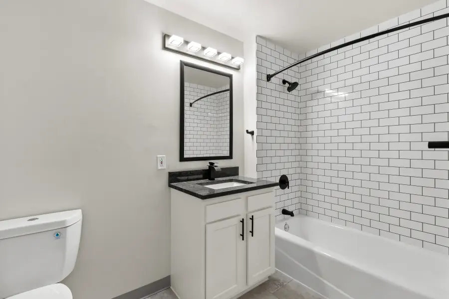 Bathroom with a subway-tiled tub surround, black fixtures and a stone-topped vanity